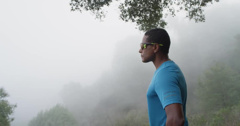 A man in sunglasses overlooks a foggy hillside