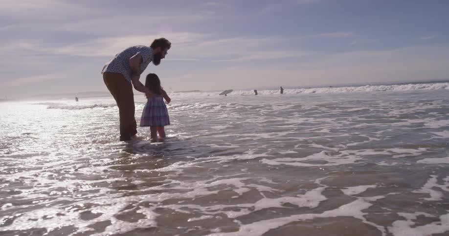 A man and young girl stand on the beach as the tide rolls in