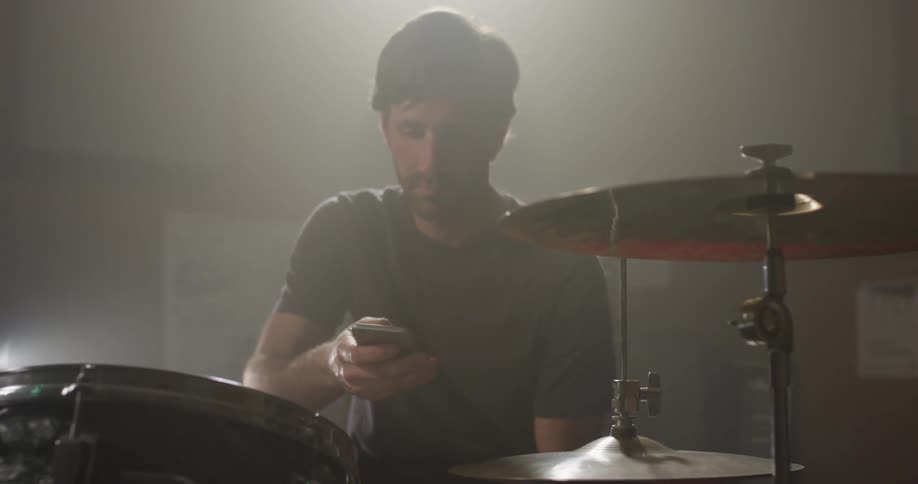 A man uses his phone as he sits at the drum kit