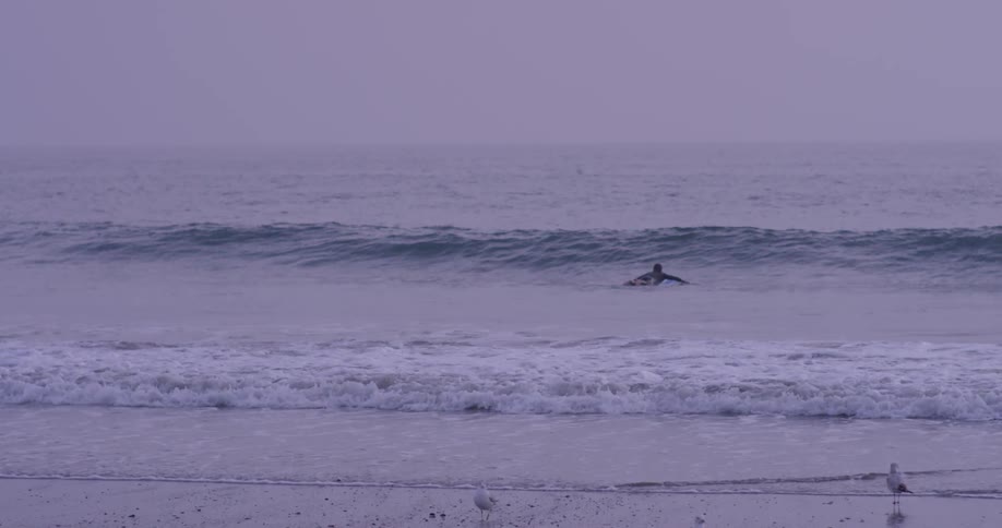 A surfer wades out into the water