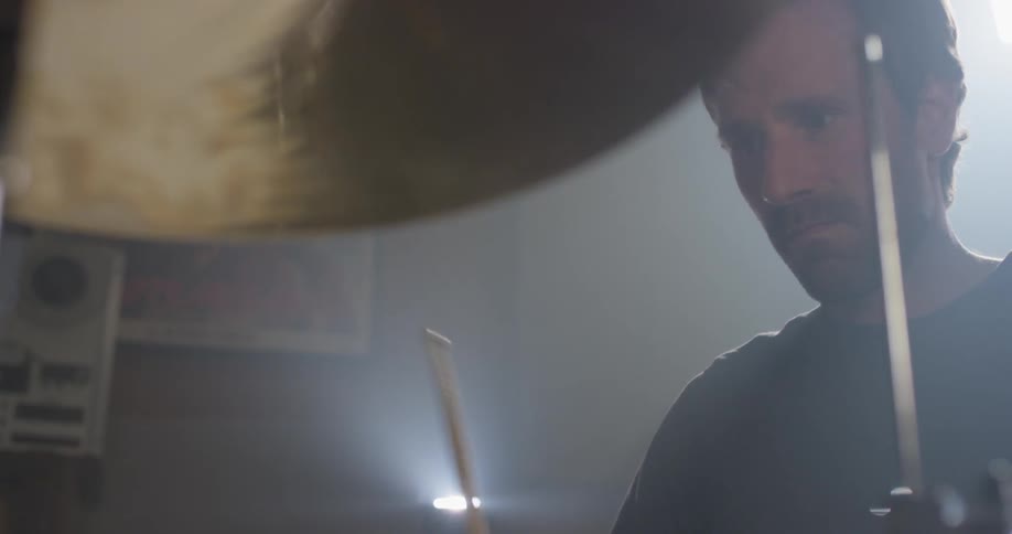 Man moves his head as he plays the drums and cymbal