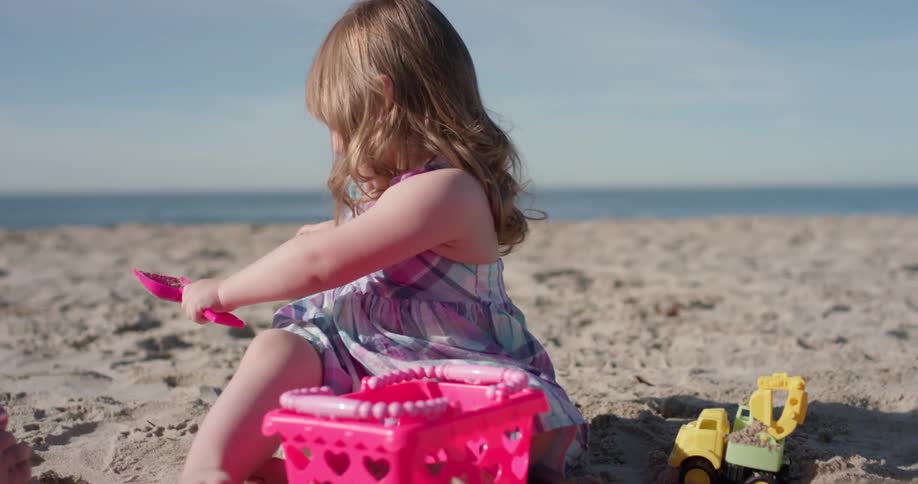 Little girl is playing in sand on ocean beach on sunny day