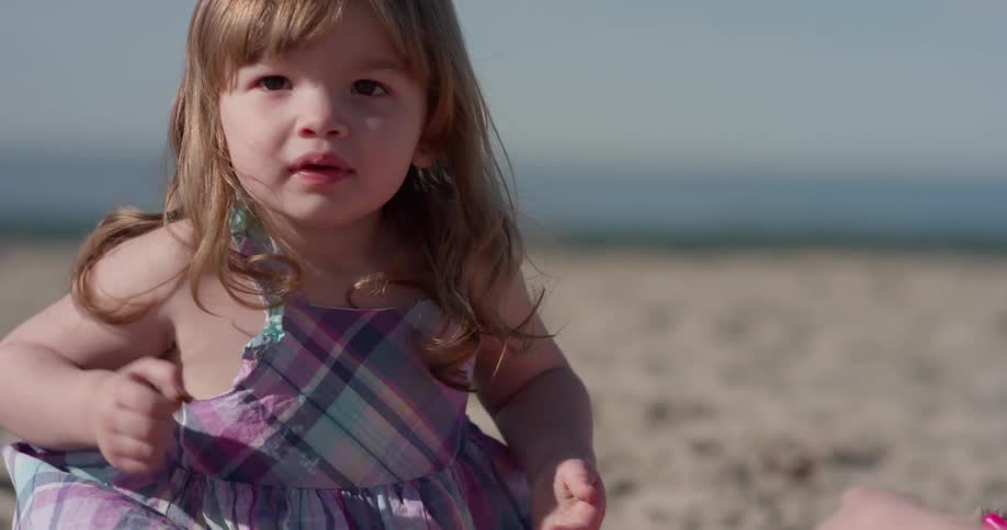 Toddler sits in the sand and throws something in the air