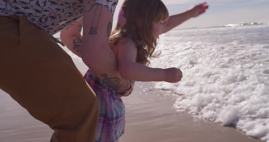 A man holds a young girl up as the tide rolls in