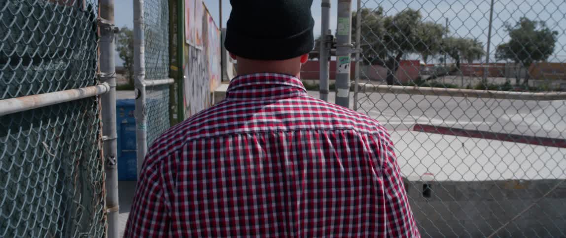 Man wearing a toque walks next to a chain link fence