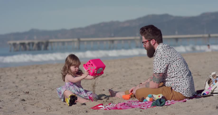 A father and daughter play with sand on a beach