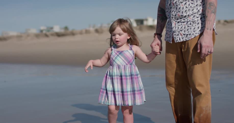 Man holds child's hand as they stand on the beach