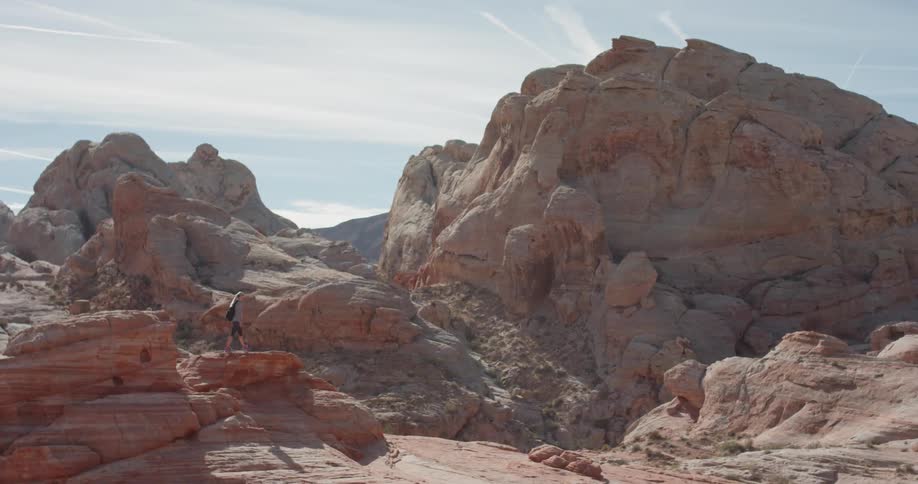 A woman climbs up and stands on a boulder in the desert
