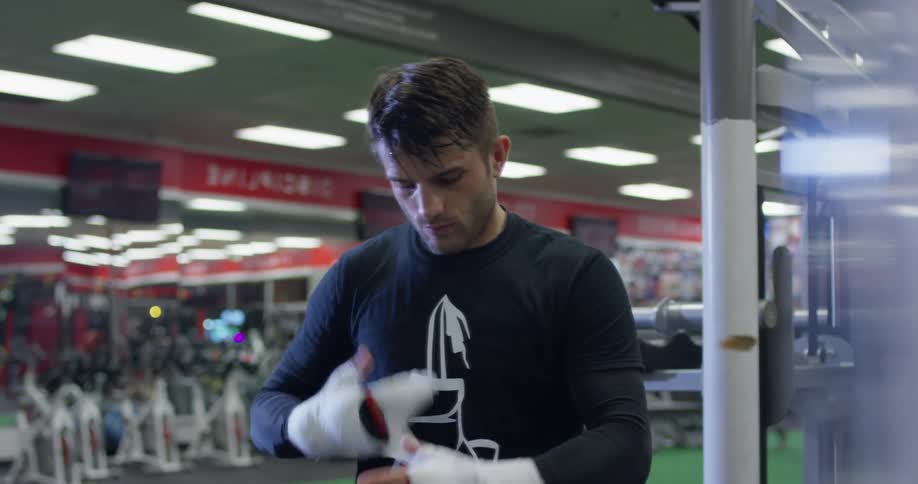 A fighter is unwrapping his hands as he stands in a gym