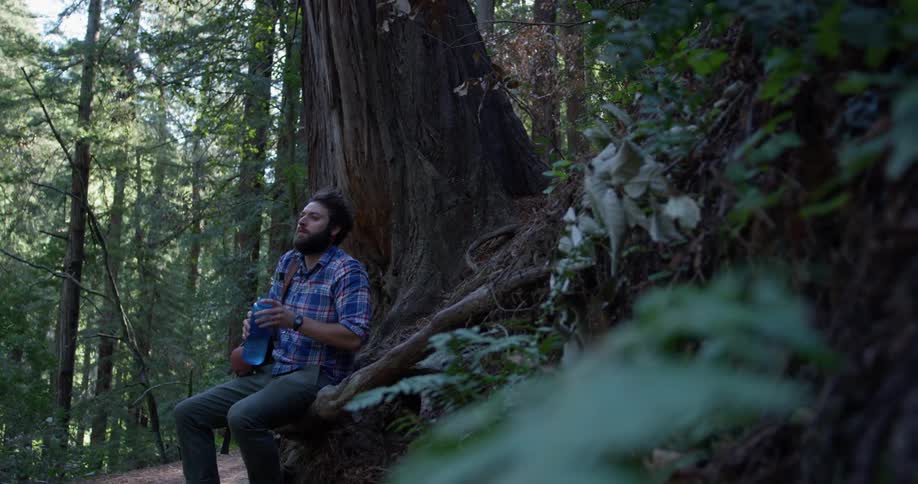 Man sits in the woods drinking from a water bottle