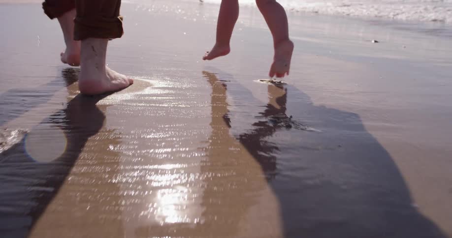 A man and young girl run on the wet sand