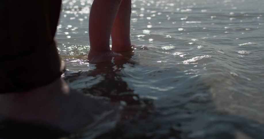 The tide rolls over the feet of a man and child