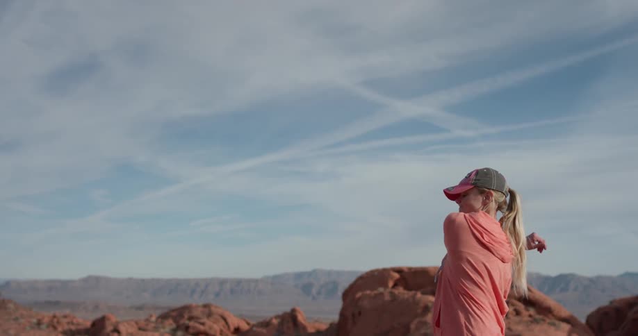 Woman stands stretching her arms outside looking out over rocky hills