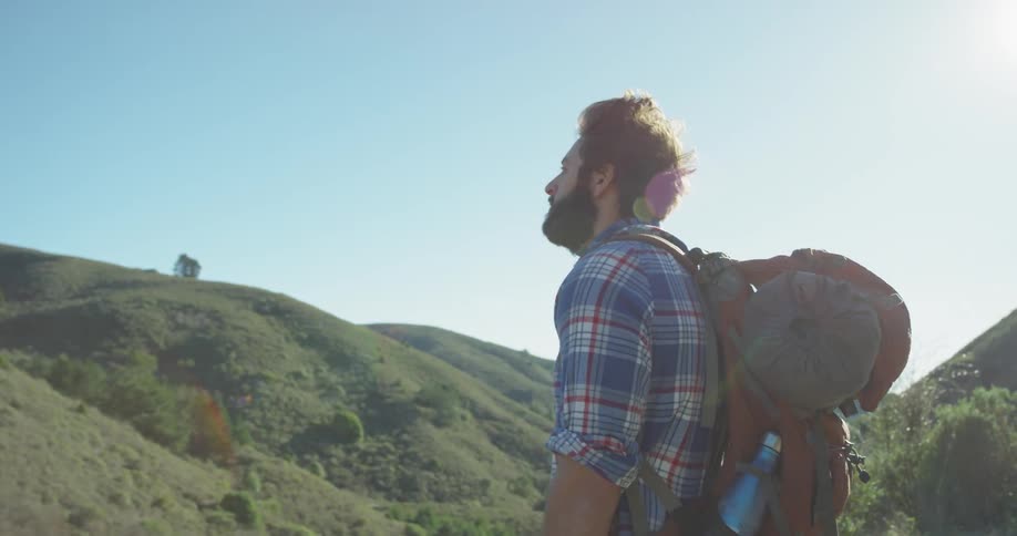 A hiker stands on the hill holding his backpack