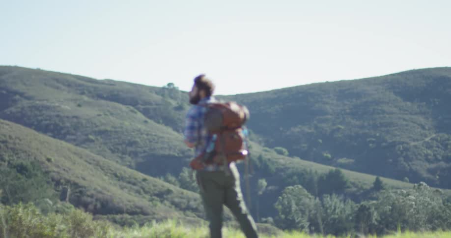 A hiker stands on the hill holding his backpack