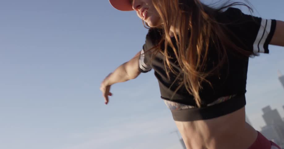 A woman in a pink hat dances on a rooftop