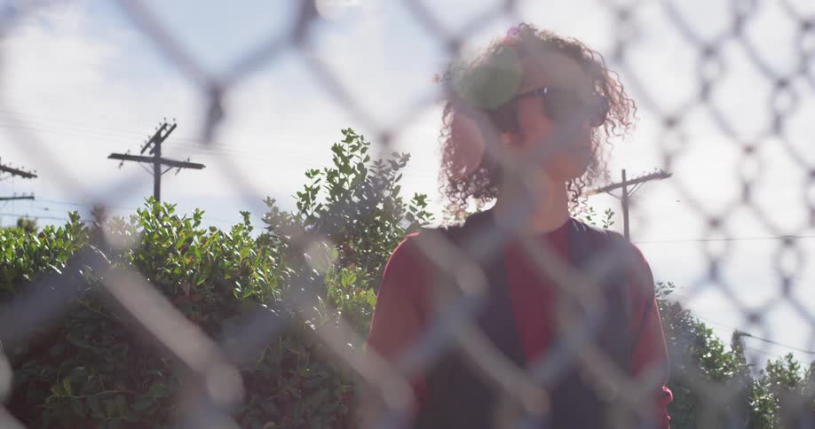 Man wearing sunglasses stands near a chain link fence