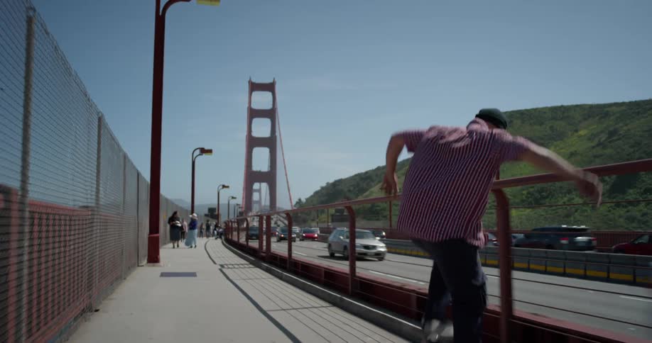 A man skateboards on the pedestrian path across the bridge