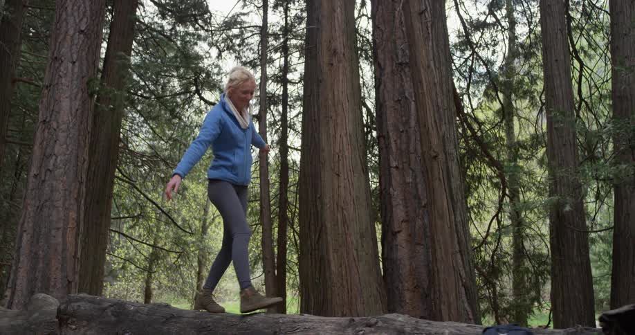 A woman balances on a fallen tree in a forest