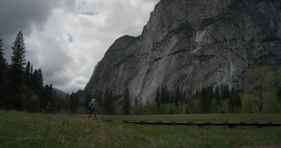 Woman walks in a grassy field toward a large mountain