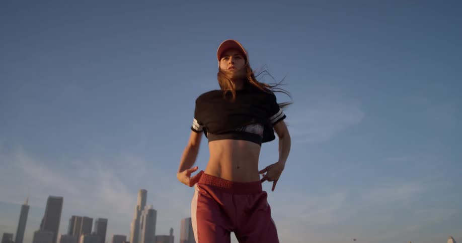 A woman in a pink hat dances on a rooftop