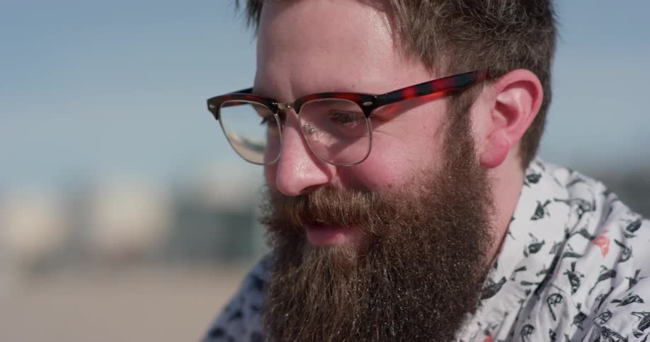 A man with a thick beard smiles and talks outside