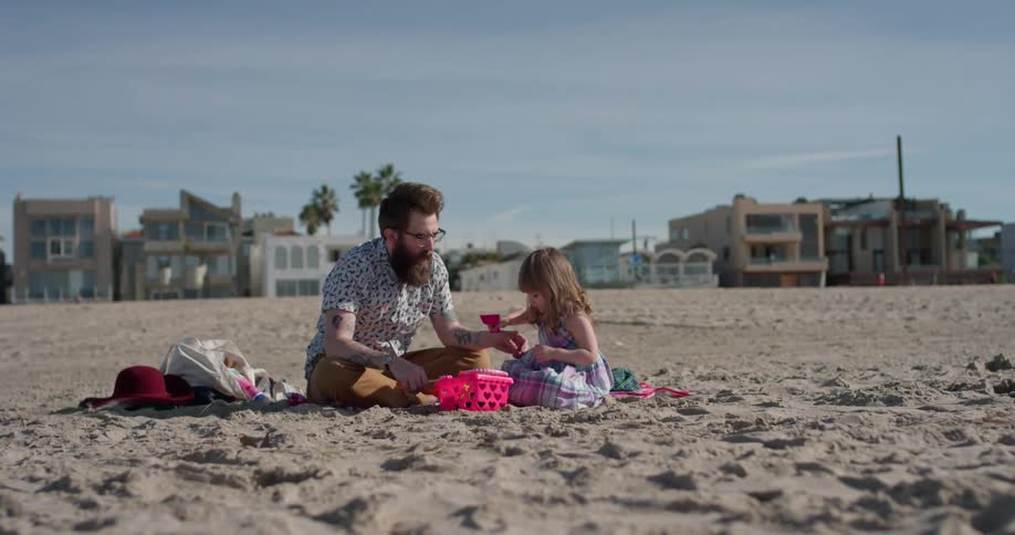 A man and young girl play on the beach