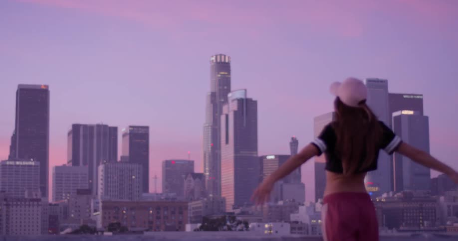 A woman in a pink hat out stretches her arms on a building rooftop
