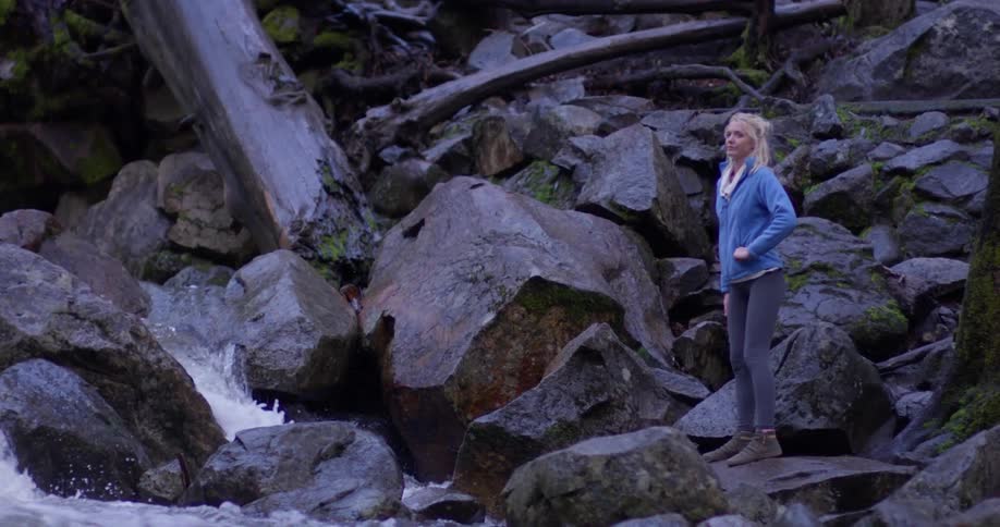 A woman stands on the rocks by the stream