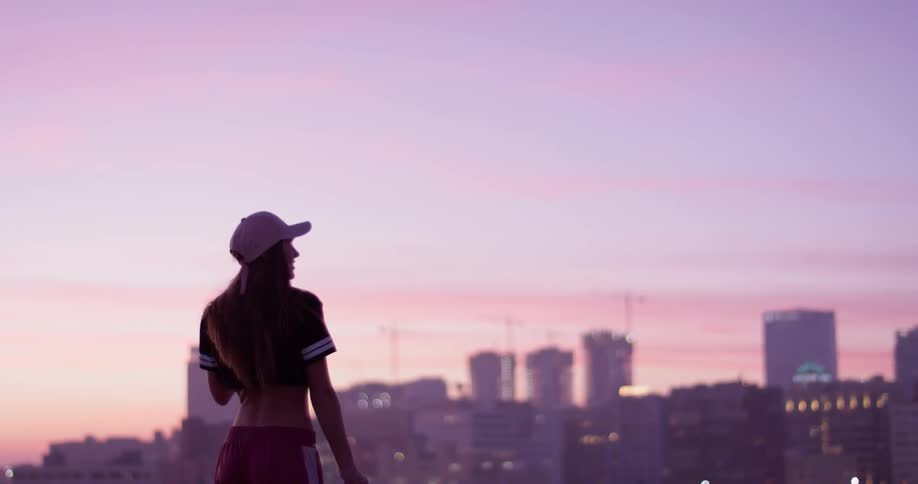 A woman is standing on a rooftop at dawn taking in an urban view