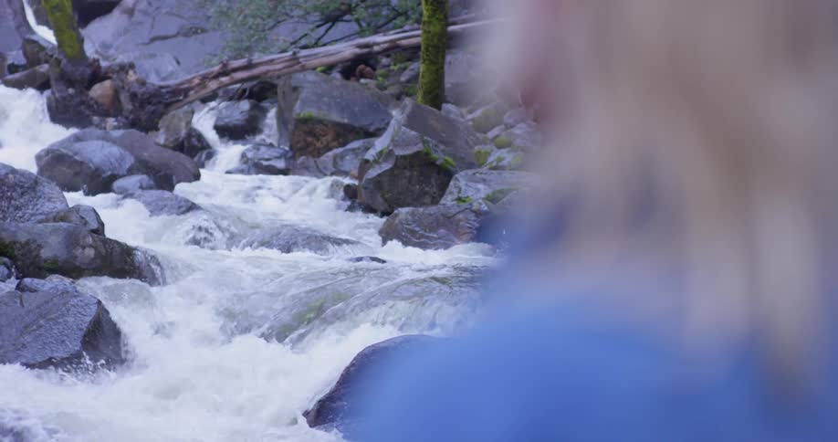 A woman stands next to a gushing river