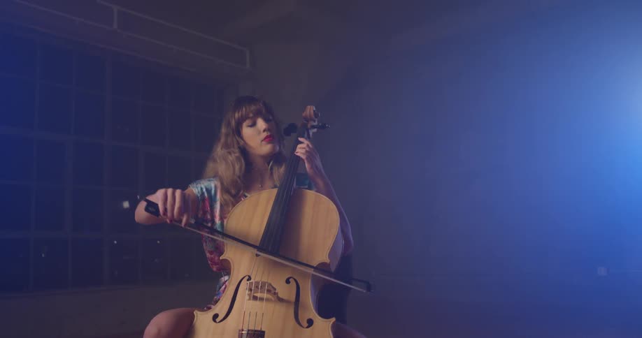 A woman plays a cello in a dim room