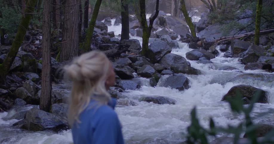 A woman stands next to a river in a forest