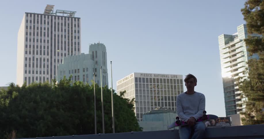 A man sits on a wall holding a skateboard in an urban setting in daylight