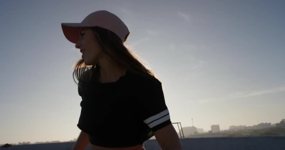 A woman in a pink hat dances on a rooftop