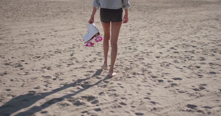 A woman carries skates on a sandy beach