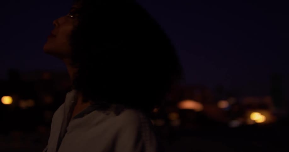 A woman stands outside in a city at dusk