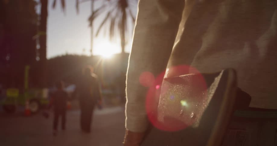 A man is carrying a skateboard as he walks outside in the afternoon