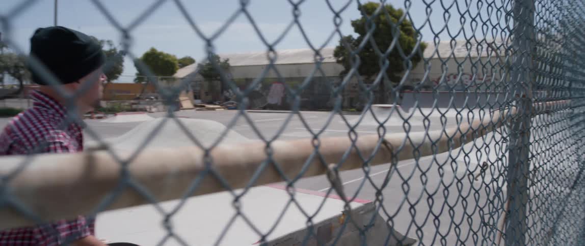 The man walks past the fence with a skateboard
