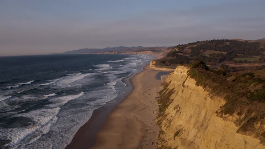 Ocean flows to a sandy shore at sunset