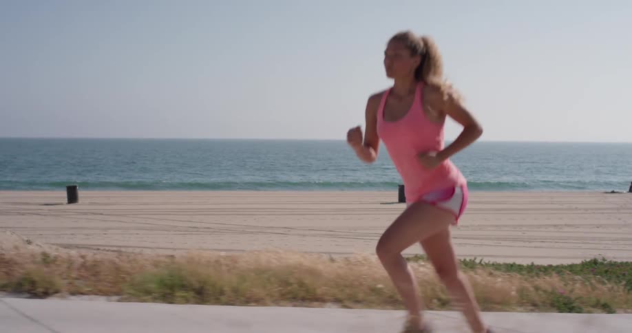Woman jogs on a sidewalk next to the beach