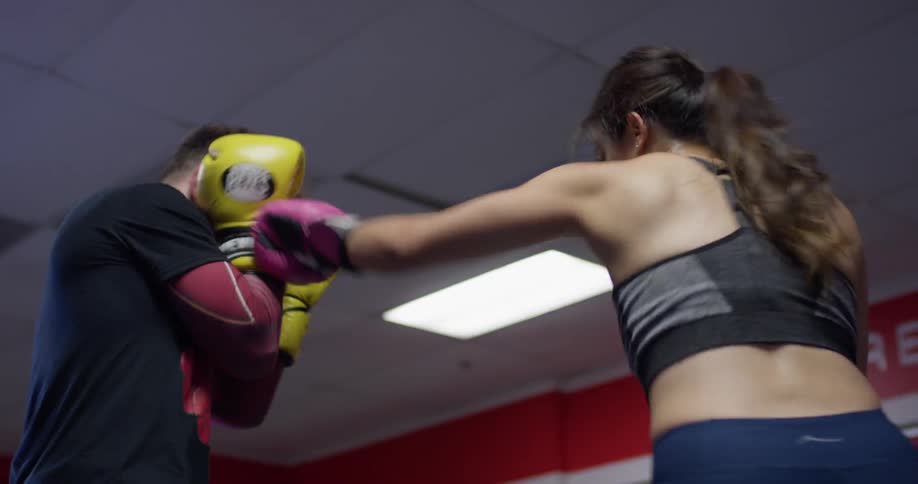 Woman practices boxing with a man in a boxing ring