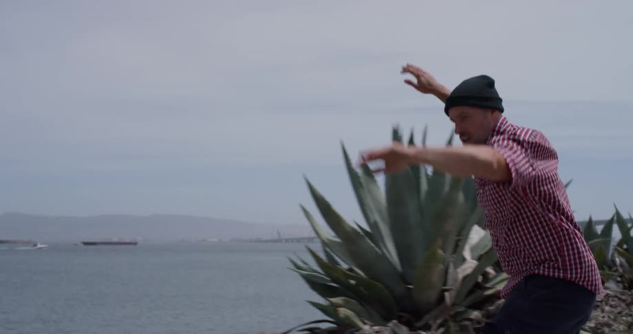 Man wearing a toque travels with his arms up next to the ocean