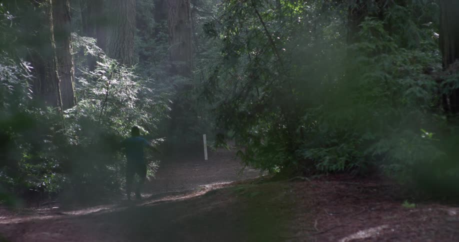 The man runs down the trail towards the forest