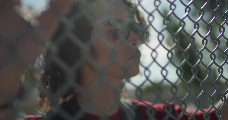 A man holds onto and looks through a chain link fence