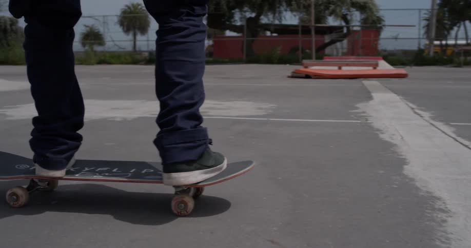 Person riding and flipping skateboard at sunny skatepark