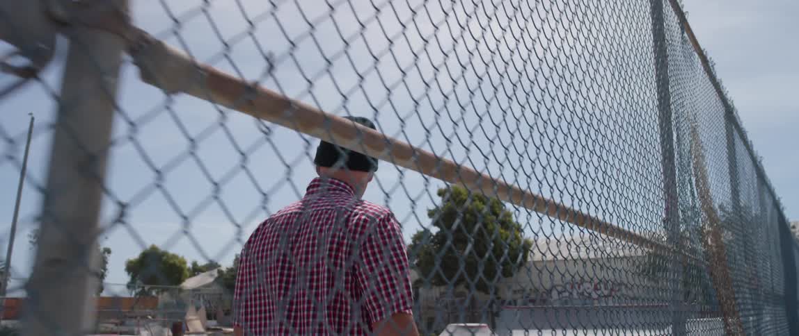 A man enters through a chain link fence opening