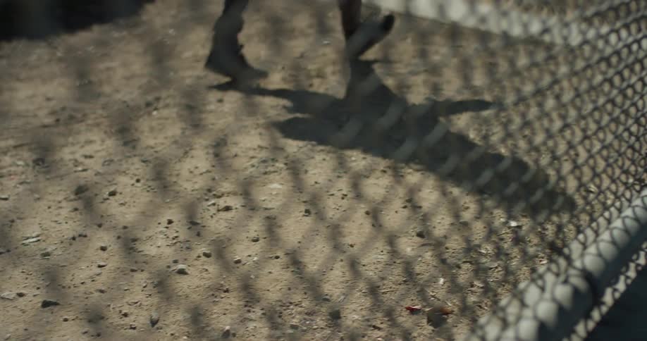 Man wearing boots walks near a chain link fence