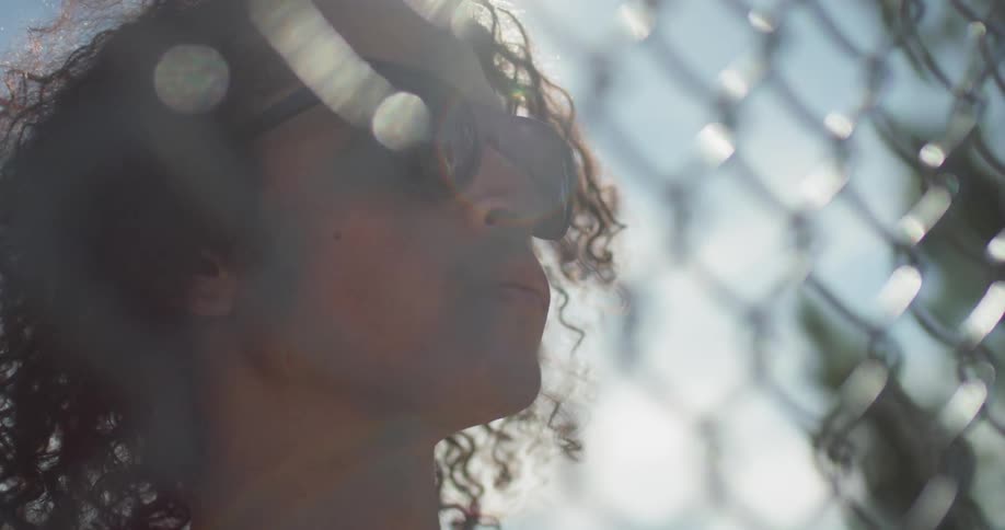 Man wearing sunglasses looks through a chain link fence on a sunny day