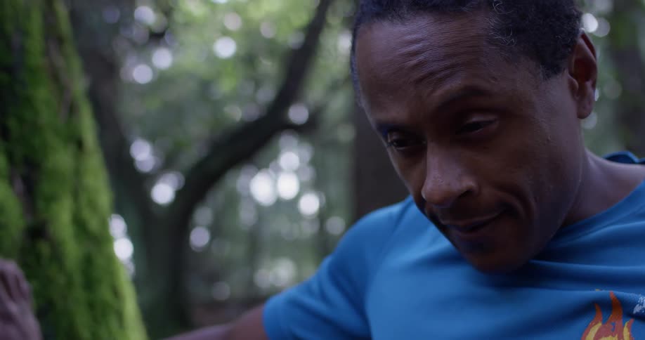 Man takes his glasses off while looking down outside in the woods